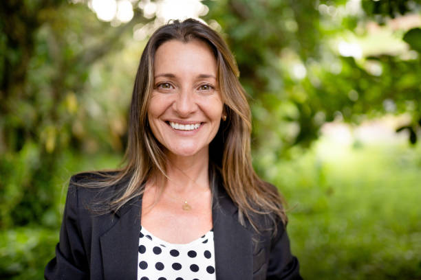 Portrait of a smiling mature woman standing alone outside in a tree-filled public park in summer